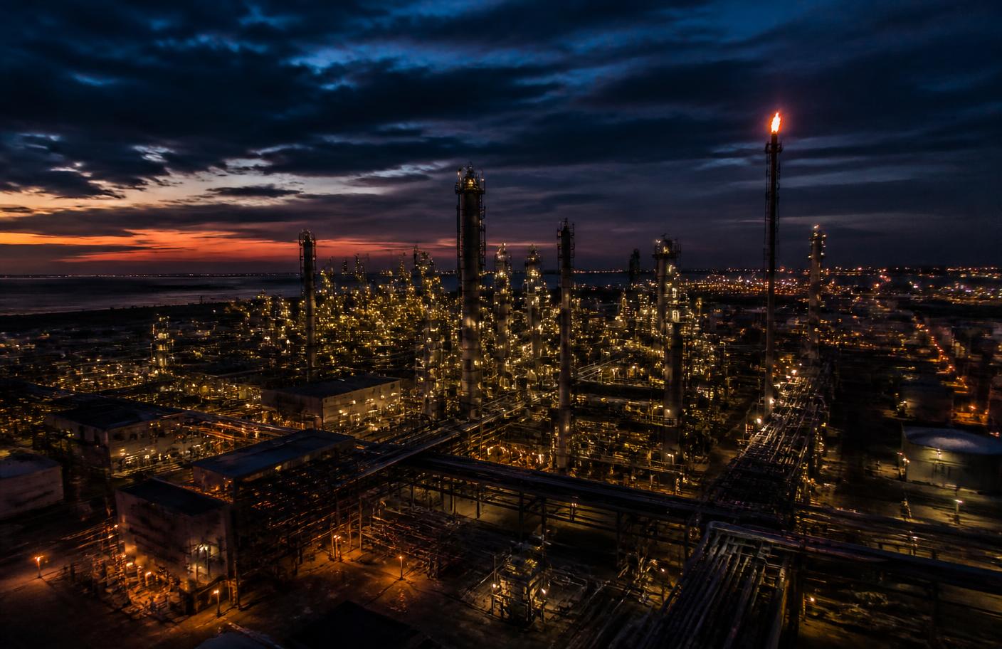 Oil refinery at dusk with distillation columns and a lit flare stack